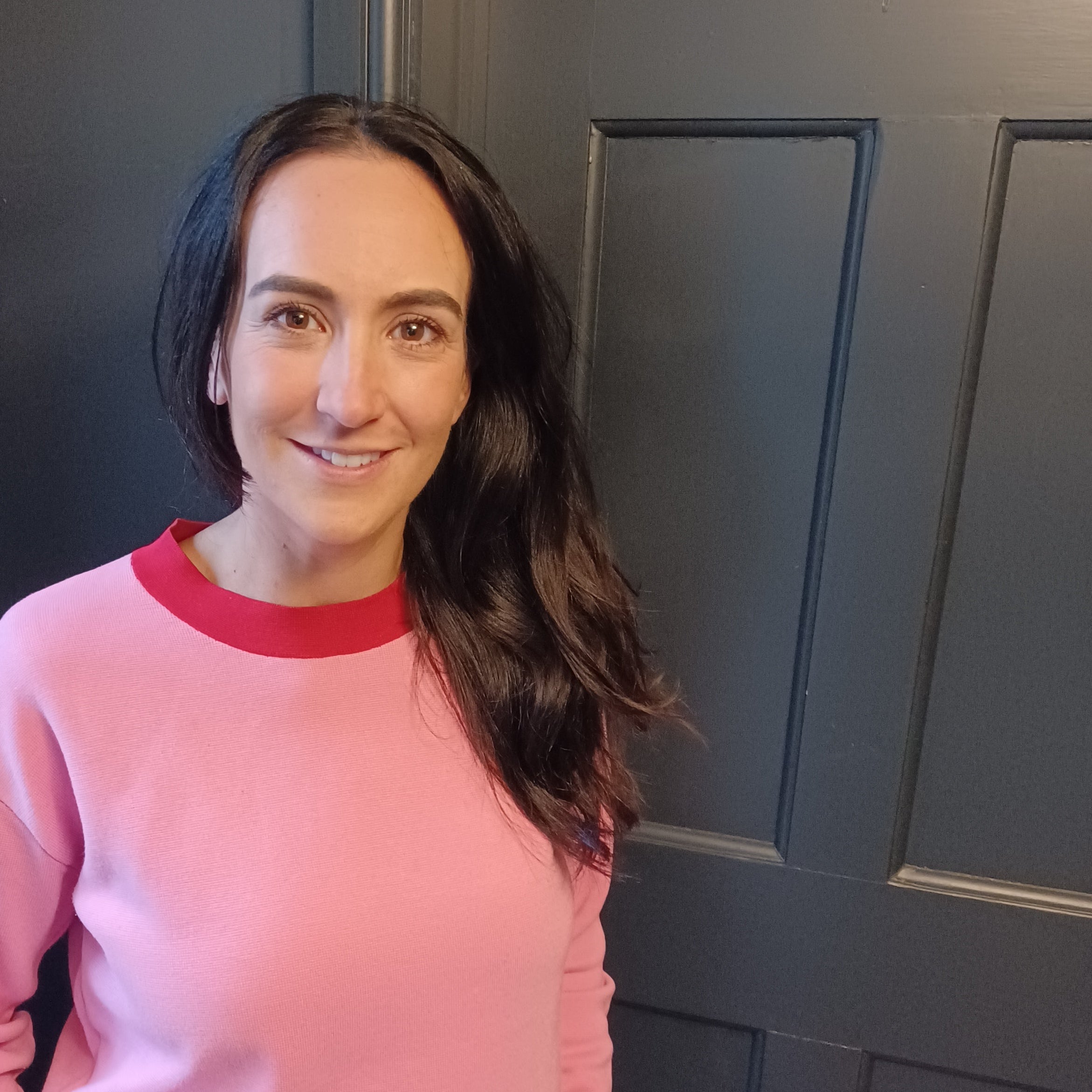 Woman wearing a pink and red sweater standing in front of a dark blue door.